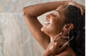 Jeune femme souriante profitant d'une douche chaude relaxante dans une salle de bain zen avec des plantes, illustrant la gestion du stress par l'hydrothérapie. Comment gérer le stress