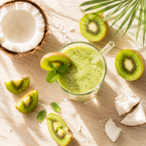 Verre de smoothie vert pastel onctueux entouré de kiwis coupés, d'un demi-avocat et d'un carnet de rituels.