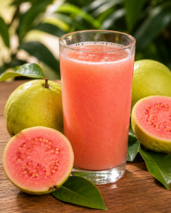 Un verre transparent rempli de jus de goyave rose frais à côté de goyaves entières coupées en deux